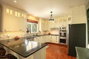 Kitchen with stainless steel appliances, a kitchen bar, a peninsula, hanging light fixtures, and glass fronted cabinets