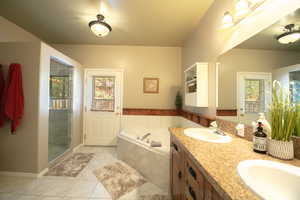Primary bathroom featuring double vanity, light tile patterned floors, a bath, and a shower stall