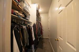 Primary walk in closet with dark colored carpet
