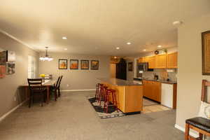 Kitchen featuring an island bar, dark countertops, light carpet and a textured ceiling. There is no dishwasher in the basement kitchen. There is only a mini fridge for cold item storage.