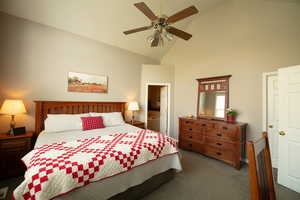 Bedroom with lofted ceiling, dark carpet, a ceiling fan, and connected bathroom