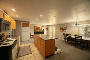 Kitchen featuring light carpet, electric stove, stainless steel microwave, and a center island.