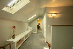 Corridor featuring a skylight, vaulted ceiling, and light colored carpet
