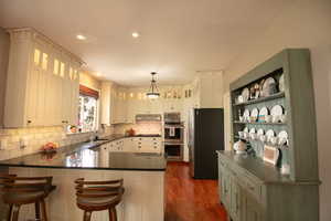 Kitchen featuring a peninsula, stainless steel appliances, white cabinetry, tongue and groove oak hardwood finished floors, and pendant lighting