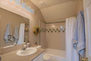 Bathroom featuring vanity, shower / tub combo, and lofted ceiling