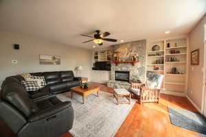 Living room with ceiling fan, tongue and groove oak hard wood finished floors, a stone fireplace, recessed lighting, and built in shelves