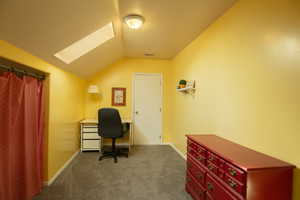Office area featuring a skylight, dark carpet, and vaulted ceiling