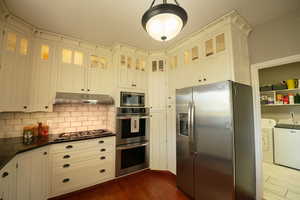 Kitchen with stainless steel appliances. Washing machine and clothes dryer Seen in the background is in another room. Laundry room has a linen closet, counter for folding clothes and separate sink. Tongue and groove wood floor in kitchen along with tastef