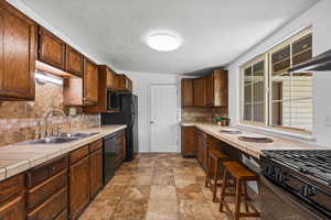 Kitchen with tile counters, black appliances, light stone finish floors, range hood, and a textured ceiling