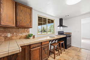 Kitchen featuring tile countertops, gas stove, wood finish cabinetry, and tasteful backsplash