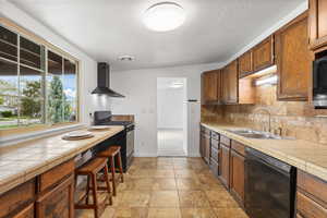 Kitchen with tile counters, black appliances, light stone finish floors, backsplash, and wood finish cabinetry