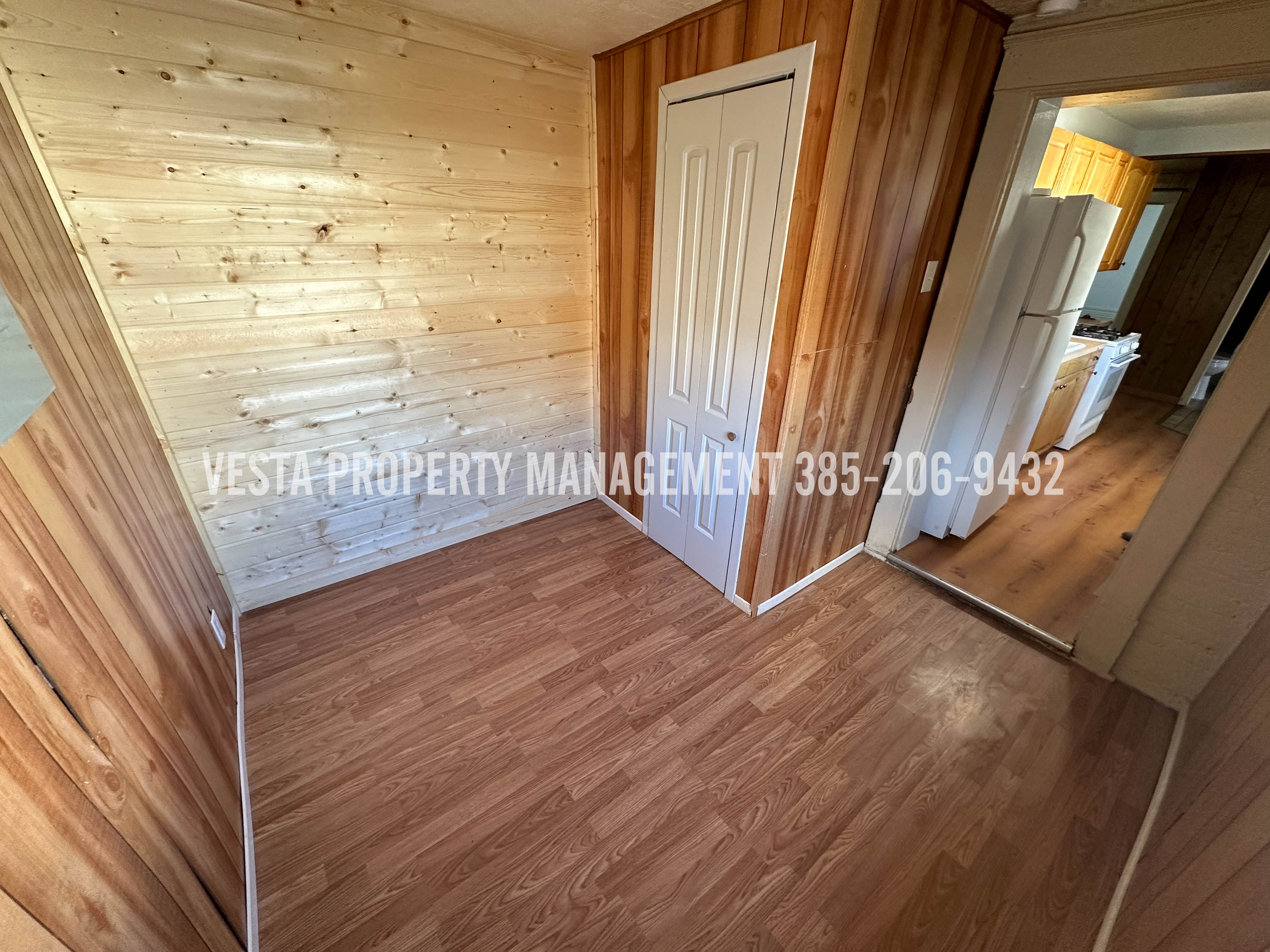 Unfurnished bedroom with wood walls, a closet, freestanding refrigerator, and wood finished floors