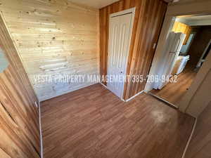 Unfurnished bedroom with wood walls, a closet, freestanding refrigerator, and wood finished floors