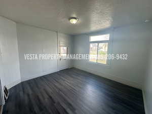Unfurnished bedroom with a textured ceiling, dark wood-style flooring, and wooden walls
