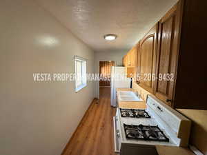 Kitchen with white appliances, light countertops, a textured ceiling, wood finish cabinetry, and light wood-type flooring
