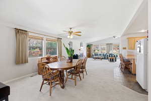 Dining space with light carpet, a ceiling fan, vaulted ceiling, and a fireplace