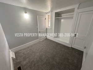 Unfurnished bedroom featuring a textured ceiling, dark colored carpet, and a closet
