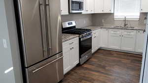 Kitchen featuring stainless steel appliances, white cabinets, light stone counters, and dark wood-type flooring