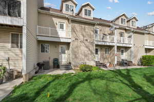 Rear view of house featuring entry steps, a patio, and a lawn