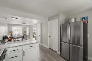 Kitchen featuring stainless steel appliances, open floor plan, light wood-type flooring, a peninsula, and white cabinets