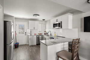 Kitchen featuring a peninsula, light stone countertops, white cabinets, stainless steel appliances, and a textured ceiling