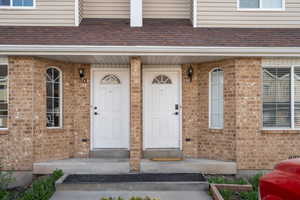 Doorway to property with brick siding, covered porch, and a shingled roof