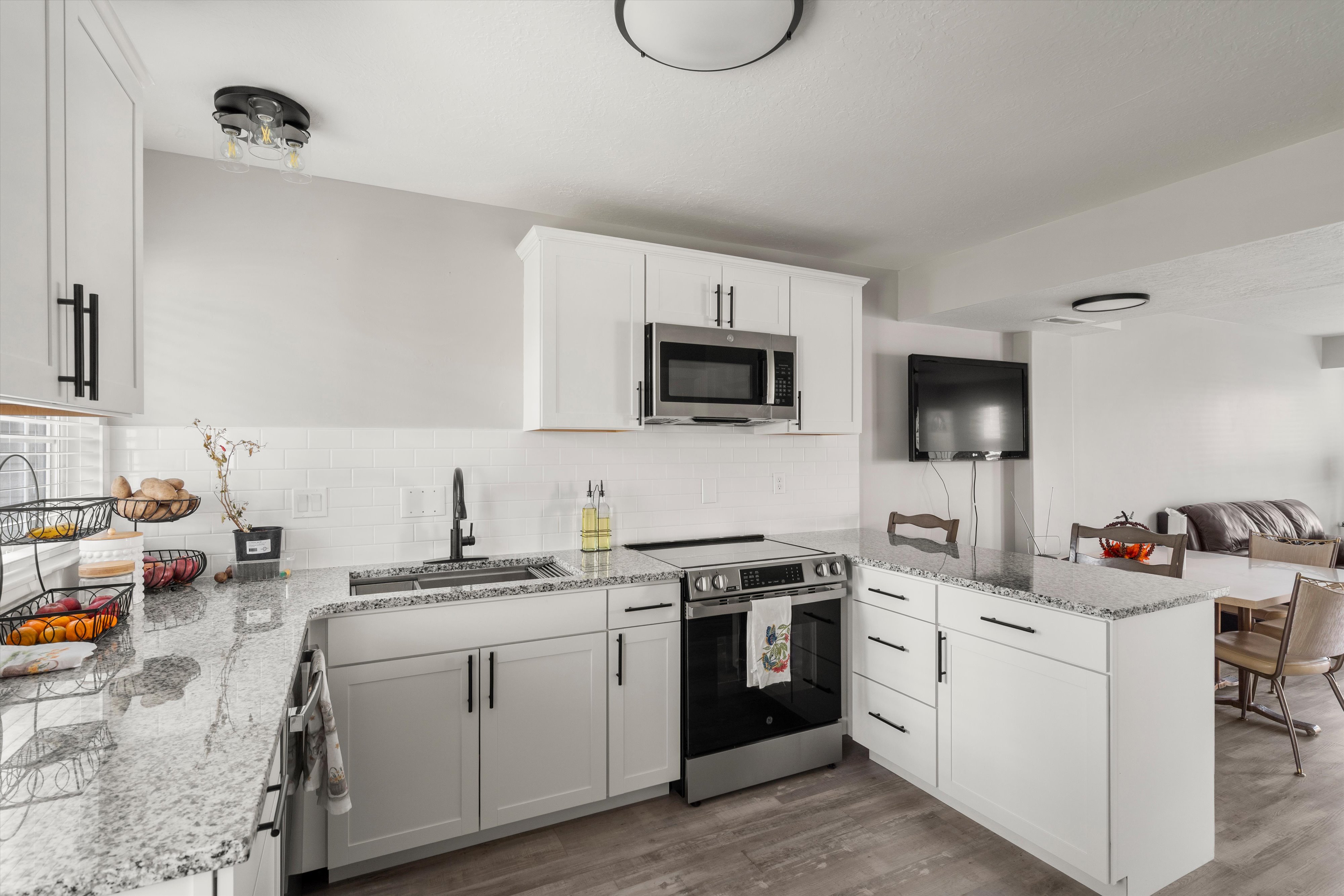 Kitchen featuring a peninsula, light stone countertops, stainless steel appliances, and white cabinetry