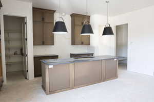 Kitchen featuring an island with sink, hanging light fixtures, wood finish cabinets, and concrete floors