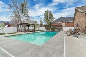 View of swimming pool with an outdoor living space, a gazebo, patio surround, and a fenced backyard