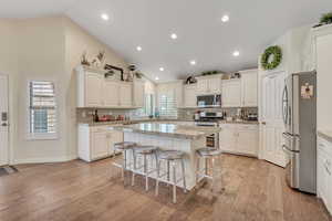 Kitchen featuring a breakfast bar, stainless steel appliances, vaulted ceiling, white cabinets, and light wood-type flooring