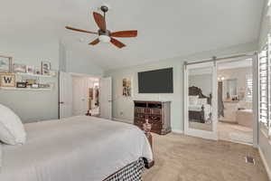 Bedroom featuring a barn door, light carpet, vaulted ceiling, ensuite bath, and ceiling fan