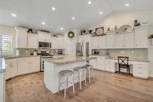 Kitchen with backsplash, a breakfast bar area, white cabinets, stainless steel appliances, and vaulted ceiling