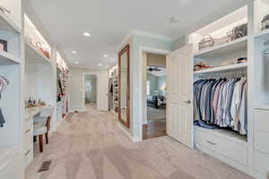 Walk in closet featuring light colored carpet, built in desk, and a ceiling fan