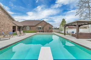 View of pool with outdoor furniture, patio surround, a fenced backyard, a diving board, and a gazebo