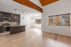 Kitchen with dark wood finish cabinetry, stainless steel appliances, beam ceiling, tasteful backsplash, and a center island with sink