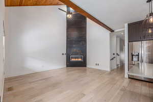 Living room with lofted ceiling with beams, light wood-style floors, and a large fireplace