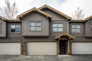 View of front of house with board and batten siding, an attached garage, and stone siding