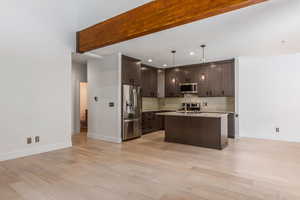 Kitchen featuring dark wood finish cabinetry, stainless steel appliances, decorative light fixtures, an island with sink, and light wood-style flooring