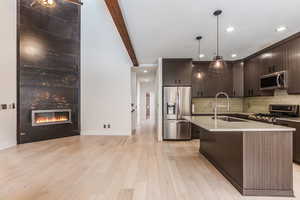 Kitchen featuring stainless steel appliances, beam ceiling, dark wood finish cabinets, a kitchen island with sink, and hanging light fixtures