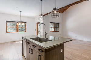 Kitchen featuring light wood-style flooring, pendant lighting, a center island with sink, vaulted ceiling, and plenty of natural light