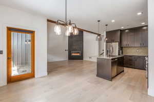 Kitchen featuring dark wood finish cabinetry, pendant lighting, tasteful backsplash, an island with sink, and light wood finished floors