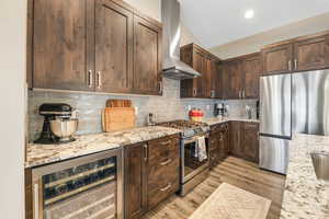 Kitchen featuring beverage cooler, dark wood finish cabinetry, stainless steel appliances, backsplash, and light wood-style floors