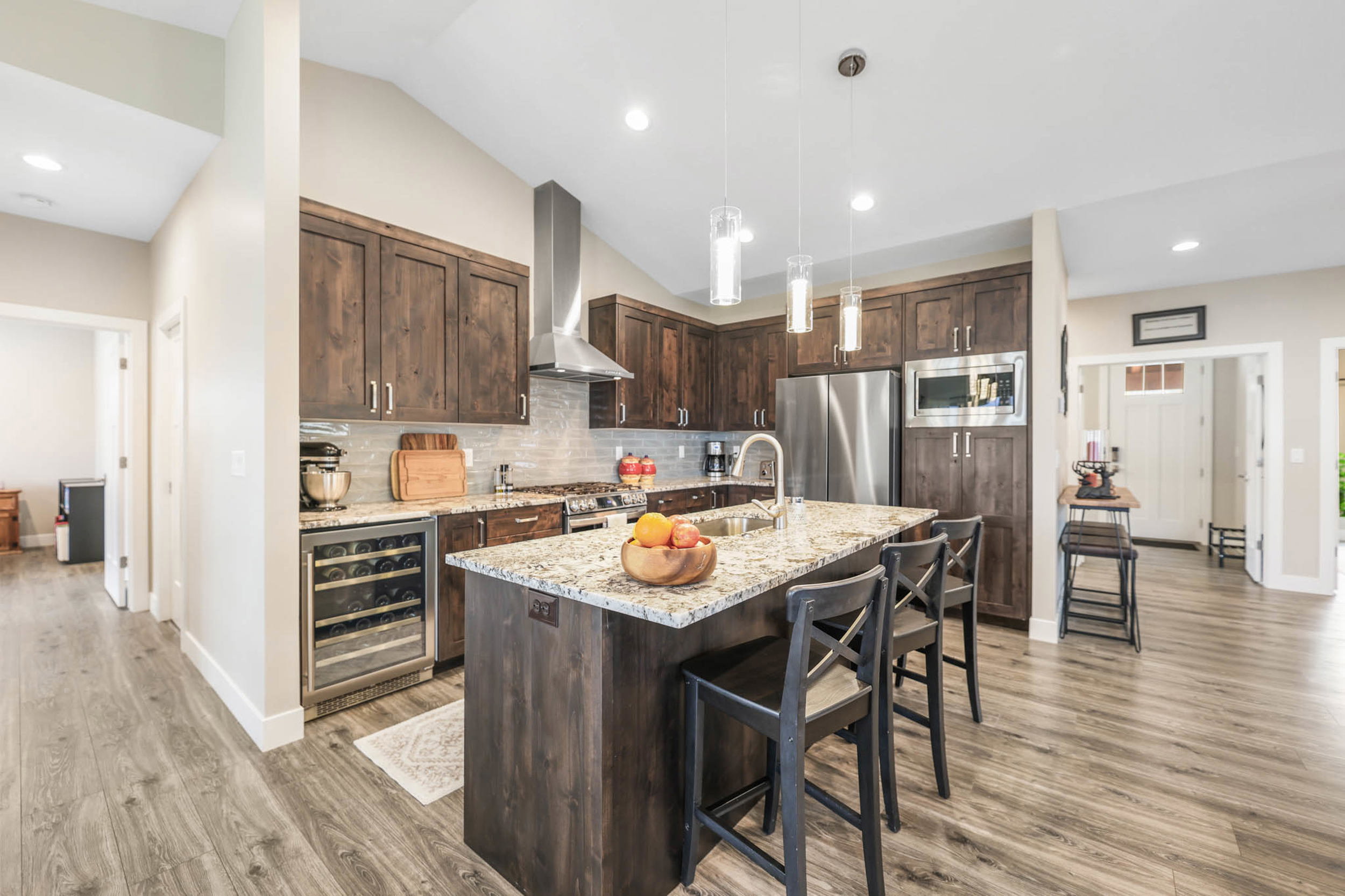 Kitchen featuring dark wood finish cabinets, light stone counters, beverage cooler, stainless steel appliances, and a kitchen bar