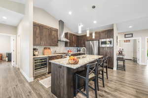 Kitchen featuring dark wood finish cabinets, light stone counters, beverage cooler, stainless steel appliances, and a kitchen bar
