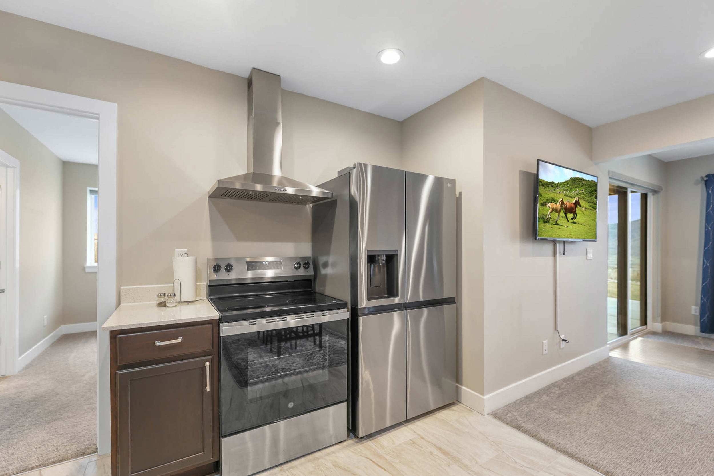 Kitchen with stainless steel appliances, light colored carpet, dark wood finish cabinetry, light stone counters, and recessed lighting