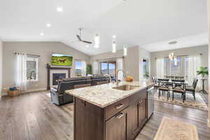 Kitchen with dark wood finish cabinetry, an island with sink, open floor plan, light stone countertops, and light wood-style floors