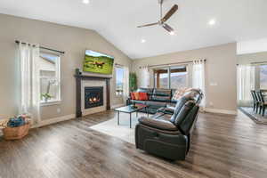 Living area with a ceiling fan, wood finished floors, recessed lighting, a glass covered fireplace, and vaulted ceiling