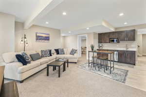 Living area with light colored carpet, beam ceiling, recessed lighting, and bar with sink