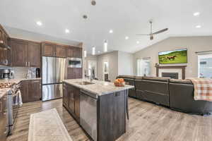 Kitchen featuring light stone counters, stainless steel appliances, open floor plan, a kitchen island with sink, and light wood-style flooring