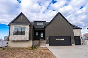 View of front of house featuring stone siding, a garage, concrete driveway, and stucco siding